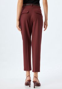 Burgunderfarbene, taillierte Hosen mit schlanker Passform, ausgestattet mit zwei Gesäßtaschen und einer glatten Textur, kombiniert mit hochhackigen Sandalen.