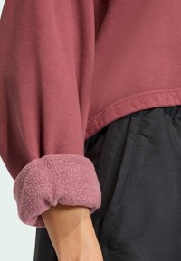 Felpa rosa polveroso con una miscela di tessuti; presenta un polsino morbido e peloso e una vestibilità rilassata. Abbinata a pantaloni leggeri neri.