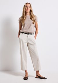 Beige tekstuuri top, valged laiad püksid, must vöö ja must võrkkangas slingback kingad. Mudel seisab käed taskutes neutraalse tausta ees.