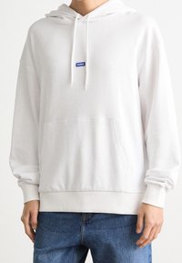 Sudadera blanca de tela de sudadera, con un bolsillo frontal, puños acanalados y un pequeño logo de marca azul en el pecho.