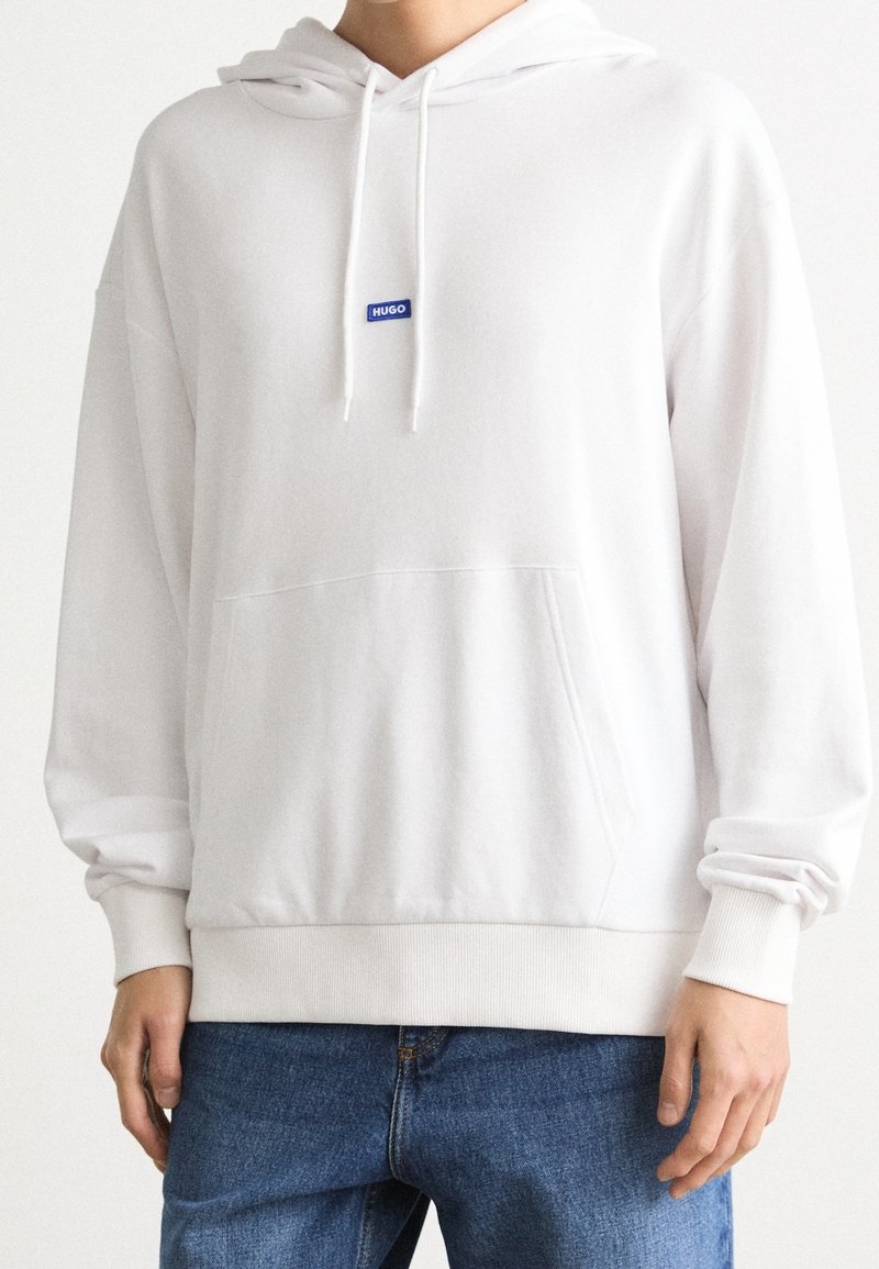Sudadera blanca de tela de sudadera, con un bolsillo frontal, puños acanalados y un pequeño logo de marca azul en el pecho.