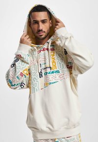 Cream-colored hoodie with a large graphic print featuring multicolored text. Soft cotton material, ribbed cuffs, and a drawstring hood.