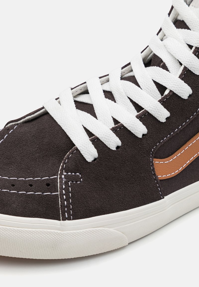 Czarne zamszowe sneakersy typu high-top z białymi sznurówkami, kontrastującym pomarańczowym paskiem po boku i białą gumową podeszwą. Widoczne szwy podkreślają detale projektu.