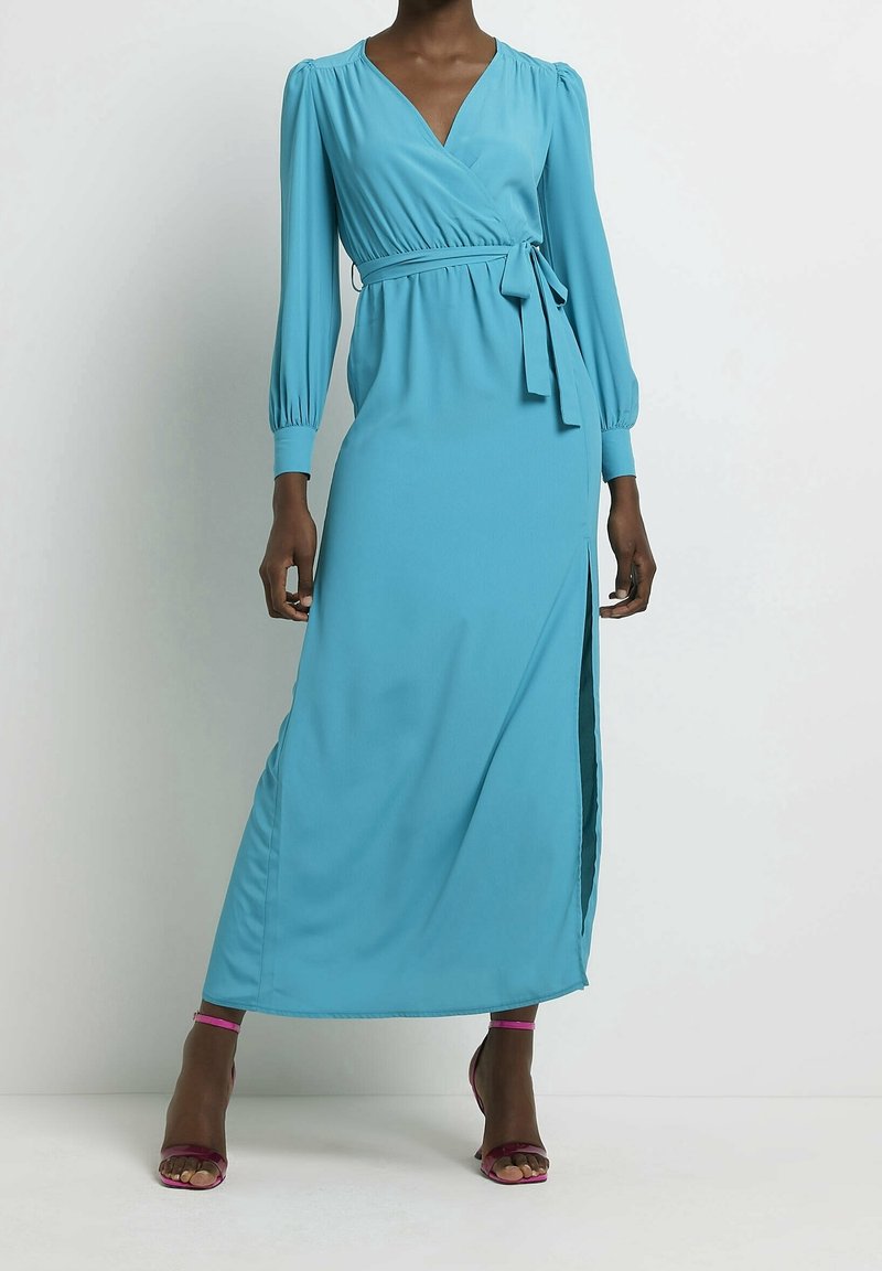 Une longue robe portefeuille couleur sarcelle en tissu lisse, avec des manches longues bouffantes, un décolleté en V, une fente latérale, agrémentée d'un détail à la taille nouée.