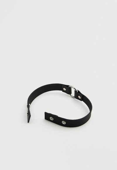 Μαύρο δερμάτινο λουράκι με ασημένια εξαρτήματα. Διαθέτει λεία υφή, κυκλικό μεταλλικό δαχτυλίδι και δύο κουμπώματα με σούστα.