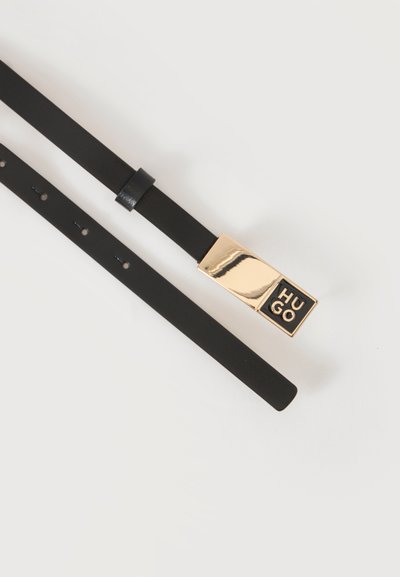 Ceinture en cuir noir avec une boucle rectangulaire dorée affichant le mot "HUGO" en lettres noires et dorées sur fond blanc.