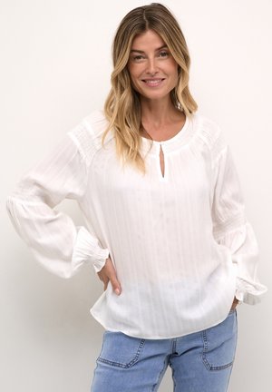 Vit blus med rund halsringning, knappringning, texturerad tyg med vertikala ränder och puffärmar med elastiska manschetter.