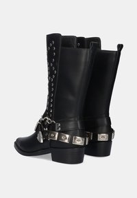 Botas altas de cuero negro hasta la rodilla con acentos de tachuelas plateadas y una correa decorativa con detalles de metal. Tacones anchos para mayor estabilidad.