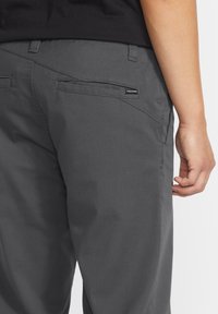 Gray trousers made from sturdy fabric featuring a slim fit, angled back pockets, and a visible logo tag on the right pocket.