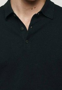 T-shirt polo noir avec un tissu texturé, doté d'un col classique, de trois boutons et d'une coupe ajustée.