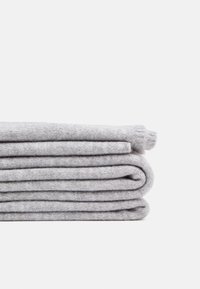 Tissu tricoté gris clair plié ou vêtement en laine empilé soigneusement sur un fond blanc uni.