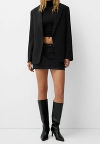 Svart oversized blazer med slag, kombinerad med en svart crop top och en denim minikjol. Höga svarta klackstövlar fulländar stilen.