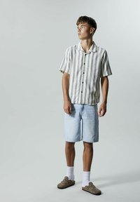 Kortermet, stripete skjorte i beige og marineblå, sammen med lyseblå denimshorts og brune slip-on-sko, med hvite sokker.