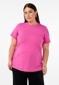 Rosa Baumwoll-T-Shirt mit kurzen Ärmeln und rundem Halsausschnitt. Hat einen lockeren Schnitt und eine glatte Textur, kombiniert mit schwarzen Hosen.