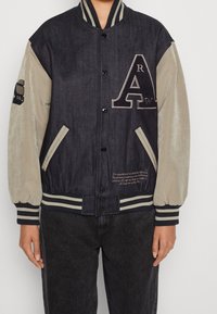 Jeansjacka i mjuk beige tyg med ribbad krage och manschetter, har logotyp och broderade detaljer på bröstet och ärmen.