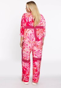 Kleurige tweedelige outfit met een levendig roze tropisch bladerenpatroon. Gemaakt van lichtgewicht stof met losse, wijde broekspijpen en een boxy top.
