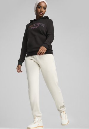 Black hooded sweatshirt with purple and orange text, paired with cream joggers. Features ribbed cuffs and pockets. White sneakers with orange accents.