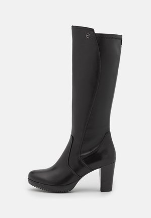 Botte haute en cuir noir avec talon bloc, bout arrondi et détail de couture latérale sur fond blanc.