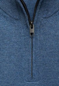 Blå stickad tröja med hög krage och dragkedja fram. Svart dragkedja ger kontrast mot tygtexturen.