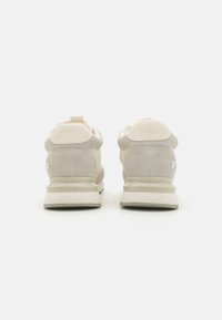 Chaussures de sport beige clair avec une tige en daim et en maille, dotées d'un col rembourré, d'un logo sur le talon et d'une semelle amortissante.