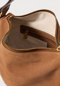 Brūns zamšs rokassomiņš ar zelta rāvējslēdzēju, bēša auduma iekšpusi un iekšējo rāvējslēdzēja kabatu ar atbilstošu zelta vilkšanas cilni.