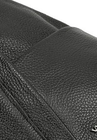 Borsa in pelle nera con finitura testurizzata, caratterizzata da un pannello liscio e dettagli cuciti su un lato. Sottile hardware metallico in accento.