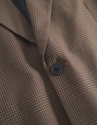 Blazer castanho com padrão, apresentando uma superfície texturizada, design de houndstooth vertical, detalhes em vermelho e um único botão preto.