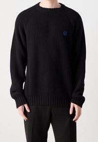 Pull en tricot noir avec poignets et ourlet côtelés. Présente un col rond et un petit logo bleu sur la poitrine. Coupe décontractée et ample.