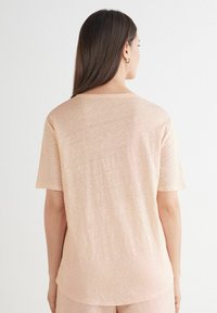 Ljus persiko-färgad t-shirt med kort ärm, lös passform, rund halsringning och mjukt, strukturerat tyg. Minimalistisk design utan synliga dekorationer.