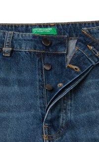 Džíny z denimu s knoflíkovým zapínáním, tmavě modrá látka, oranžové švy a zelená etiketa "United Colors of Benetton" na pasu.