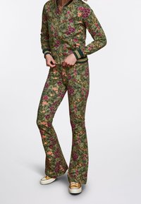Chándal floral en verde, con flores moradas y naranjas. Chaqueta ajustada con cremallera y puños de canalé, y pantalones acampanados con el mismo estampado.