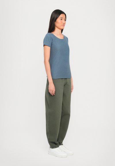 Blue textured short-sleeve top paired with loose green trousers and white sneakers; clean lines, casual fit, and neutral colors.