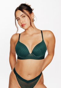 Reggiseno verde a coste con scollatura profonda e spalline sottili. Abbinato a un perizoma verde coordinato con tessuto a strisce trasparente e un taglio a vita bassa.