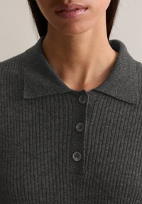 Maglione polo a coste grigio con una texture morbida, colletto classico e tre bottoni grigi lungo la placca per la chiusura.
