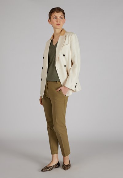 Blazer beige doppiopetto con bottoni neri, top verde oliva a scollo a V, pantaloni khaki slim-fit e ballerine nere con stampa leopardata.