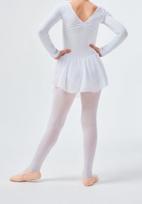 Jeune danseuse de ballet en justaucorps blanc, jupe et collants avec des chaussons de ballet pêche, debout les mains sur les hanches et les jambes écartées.