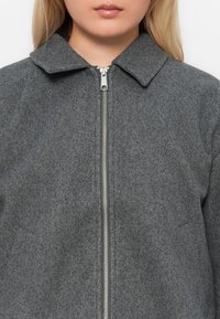Giacca grigia in misto lana con colletto, zip frontale e design essenziale. Presenta una texture morbida senza motivi visibili o dettagli hardware.