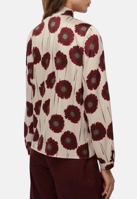 Blusa a maniche lunghe in morbido tessuto crema con motivo floreale bordeaux con centri scuri, colletto e polsini abbottonati.