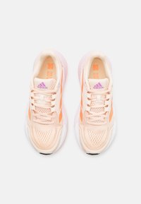 Chaussures de sport couleur pêche clair avec une tige en mesh respirant, une semelle intermédiaire blanche et des accents orange. Caractérisées par une fermeture à lacets et une surface texturée.