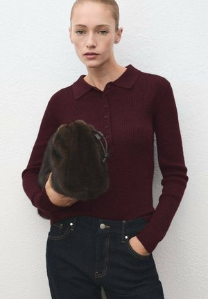 Suéter burdeos de canalé con cuello y botones, combinado con jeans de mezclilla oscuros. La modelo sostiene un bolso de piel de fur oscuro.