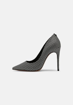 Zwart-witte dames pump met een hoge hak, voorzien van een hondentandmotief, een spitse neus en een stilettohak, op een witte achtergrond.