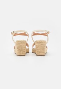 Beige espadriller med vevet jute-dekkerte blokkhæler og justerbare ankelstropper, med en glatt skinnoverdel og myk fôr.