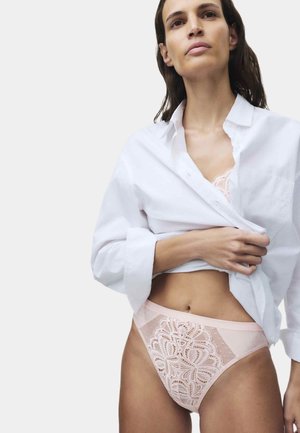 Vrouw draagt een wit overhemd dat omhoog is getild om een lichtroze kanten beha en bijpassend hoge taille kanten ondergoed te tonen.