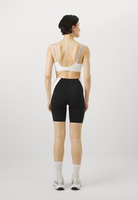 Bijeli sportski bralet s podesivim trakama i crnim visokim biciklističkim šortsevima, glatka tkanina, u minimalističkom dizajnu, prikazano sa stražnje strane.