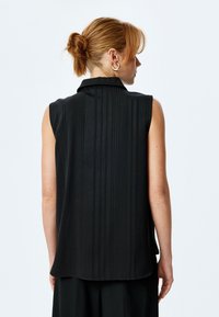 Top senza maniche nero con texture a coste verticali, dettagli sul colletto e una silhouette fluida. Tessuto liscio con una leggera lucentezza.