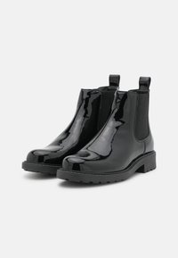 Botines Chelsea de charol negro con un acabado suave, paneles laterales elásticos y lengüetas para facilitárselo al ponérselos. Suela de goma gruesa y texturizada.