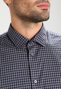 Mörkblå och grå rutmönstrad skjorta med krage som knäpps, med en strukturerad tygkvalitet och två knappar på den främre placketen.