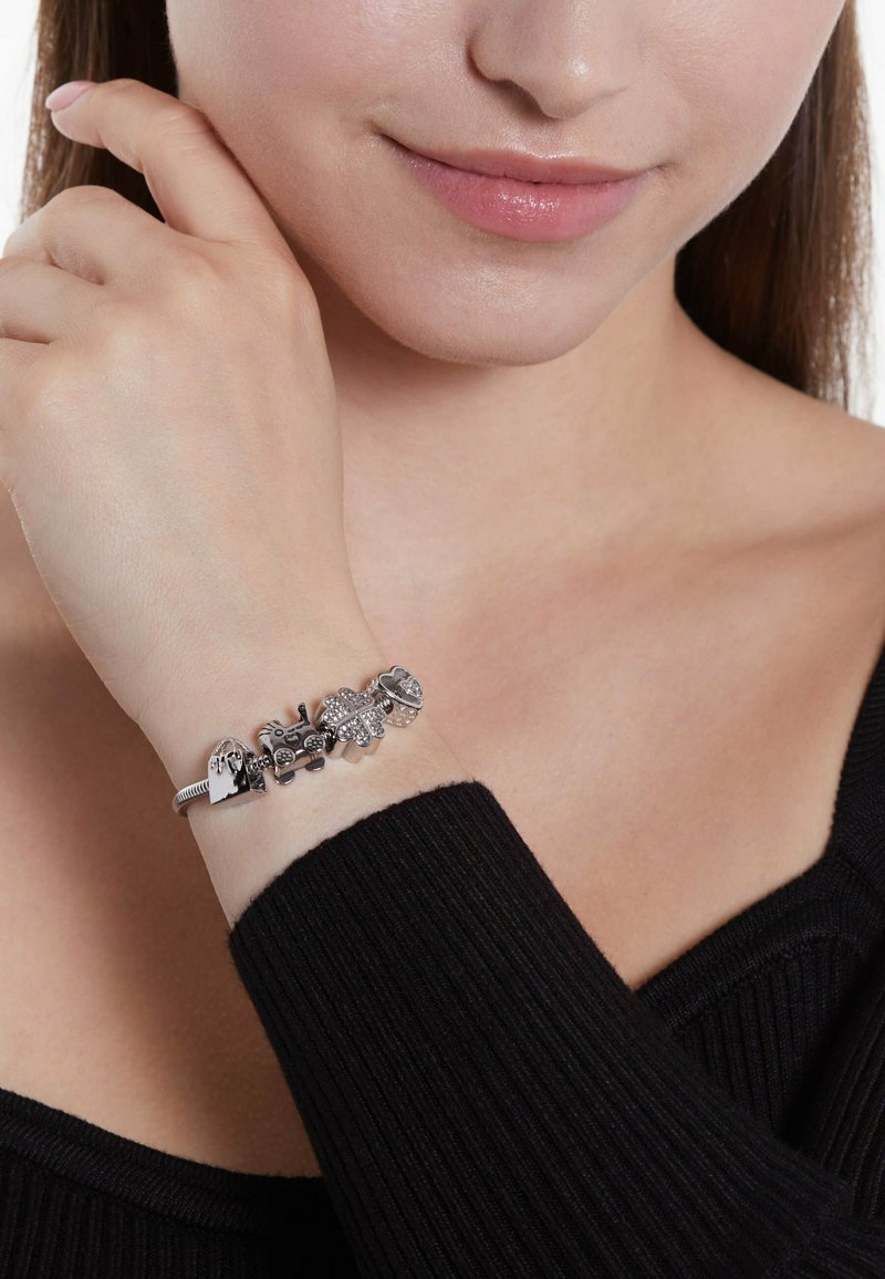 Silbernes Charm-Armband mit verschiedenen dekorativen Charms, darunter Herz- und Sternformen, auf einem nackten Handgelenk.