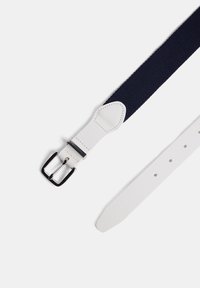 Navy elastinen vyö, jossa on valkoinen nahkainen pää ja solki. Varustettu kiiltävällä hopeanvärisellä soljella ja useilla säätörei'illä.