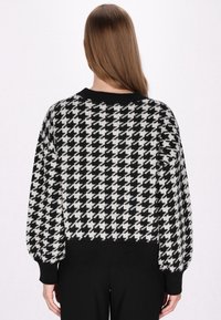 Zwart-witte oversized trui met een houndstooth patroon, geribbelde zwarte kraag en boorden, en een zachte, gestructureerde stof.